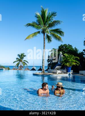 Zwei Personen entspannen sich in einem atemberaubenden Infinity-Pool mit Blick auf das Meer auf Mauritius. Umgeben von Palmen genießen sie erfrischende Getränke und die Ruhe eines perfekten Urlaubs. Ein Paar in den Flitterwochen Stockfoto