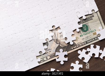 Puzzleteile umgeben eine 20-Dollar-Rechnung auf einer Holzfläche in einer Collage Stockfoto