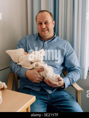 Vater hält ein neugeborenes Mädchen in weicher Kleidung. Emotionales Vaterschaftsmoment und familiäre Verbindung nach der Geburt. Stockfoto