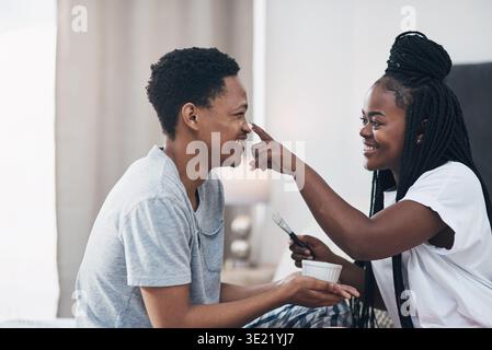 Glückliches, Hautpflege und schwarzes Paar im Schlafzimmer mit Gesichtscreme für gesunde Haut, Bindung und Wellness. Ehe, Heim und Mann mit Frau mit Gesicht Stockfoto