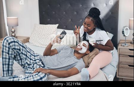 Glückliches, Selfie- und schwarzes Paar im Schlafzimmer mit Gesichtspflege, Binden und Wellness. Heirat, Haus und Foto eines Mannes mit Frau mit Maske für Stockfoto