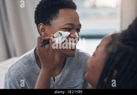 Glückliches, Hautpflege und schwarzes Paar zu Hause mit Gesichtsmaske für gesunde Haut, Bindung und Wellness. Ehe, verspielt und Mann mit Frau mit Gesichtscreme Stockfoto