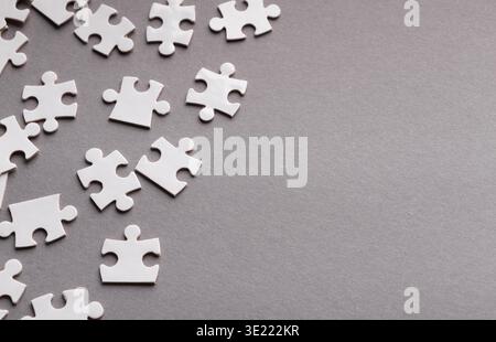 Sammlung von weißen Puzzleteilen auf einer grauen Oberfläche für ein Collage- oder Mosaikprojekt Stockfoto