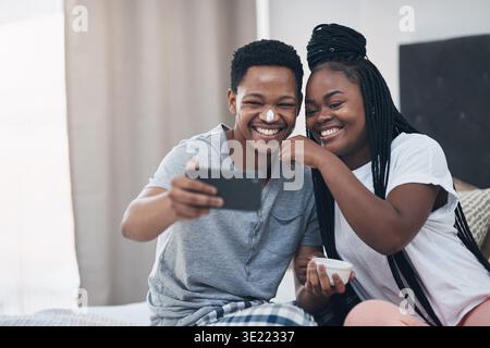 Glückliches, Selfie und schwarzes Paar im Schlafzimmer mit Gesichtscreme für Gesundheit, Bindung und Wellness. Heirat, Haus und Foto eines Mannes mit Frau mit Lotion für Stockfoto
