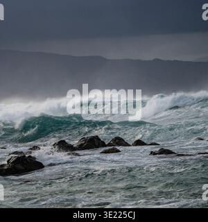 Stürmische Meereswellen stürzen unter einem dunklen, bewölkten Himmel gegen Felsen. Hookipa Beach, Maui, Hawaii, USA Stockfoto