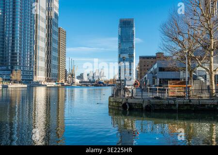 Skyline der Stadt mit Wolkenkratzern, die sich in einem ruhigen Fluss unter einem klaren blauen Himmel spiegeln. Canary Wharf, London, Großbritannien Stockfoto