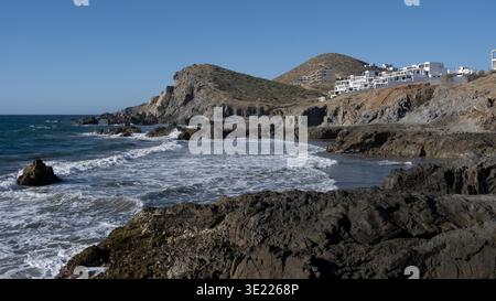 Felsige Küste mit Wellen gegen Klippen und weißen Gebäuden im Hintergrund. Todos Santos, Baja California Sur, Mexiko Stockfoto