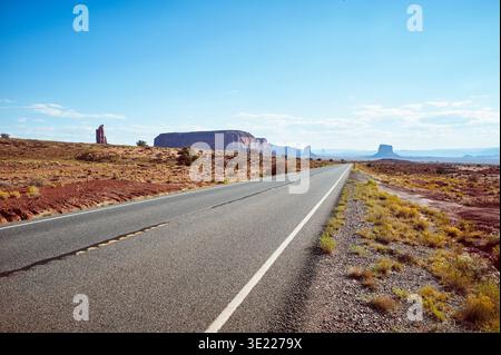 Lange Wüstenstraße, die in ferne Berge unter einem klaren blauen Himmel führt. Monument Valley, Arizona, USA Stockfoto