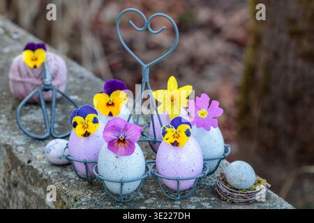 osterarrangement mit Eiern, verziert mit Bratschenblüten, Narzissen und Kerzen Stockfoto