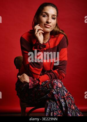 Frau in rot gestreiftem Pullover, die auf einem Stuhl mit rotem Hintergrund sitzt. Deutschland Stockfoto