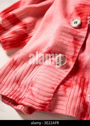 Nahaufnahme einer rosa gerippten Strickjacke mit roten Bindegürteln und großen Knöpfen. Deutschland Stockfoto