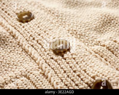 Nahaufnahme aus beigefarbenem Strickstoff mit braunen Knöpfen in vertikaler Linie. Deutschland Stockfoto