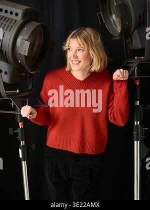 Frau in rotem Pullover lächelt zwischen zwei großen Studiolampen auf schwarzem Hintergrund. Deutschland Stockfoto