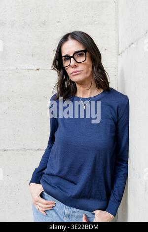 Frau mit Brille, die einen blauen Pullover trägt, steht an einer Betonwand. Mailand, Italien Stockfoto