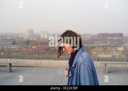 Eine junge Frau in einer Jeansjacke auf einem Dach mit einem Stadtbild im Hintergrund. Brüssel, Belgien Stockfoto