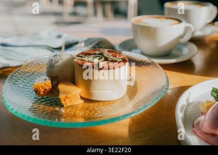 Ein Dessert und Kaffee sind in warmen Licht getaucht. Mousse mit Karamell-Auflage sitzt auf einer Glasplatte. Kleine Kekse und Garnituren begleiten die Süßigkeiten. Kaffeetassen leuchten Stockfoto