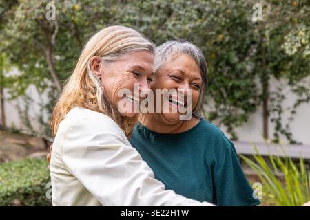 Verschiedene ältere Freundinnen umarmen sich in einem Wohngarten mit üppiger grüner Kulisse. Mitgefühl, Gesellschaft, Wellness, Freundschaft, Gelassenheit, Natur, Zuneigung || Model veröffentlicht Stockfoto