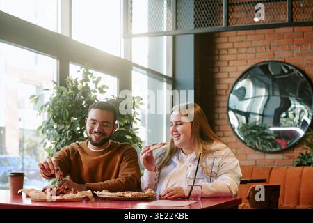 Junger Mann und Frau lachen, während sie Chicken Wings am Cafe Table teilen Stockfoto
