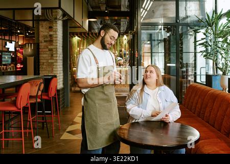 Junge Frau, die Essen von einem Mann mittleren Alters bestellt, der im Restaurant Kellner ist Stockfoto
