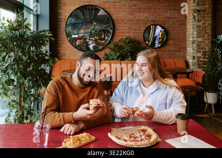Junger Mann und Frau genießen Pizza und lachen zusammen drinnen Stockfoto