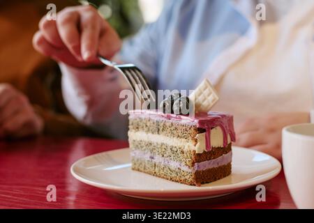 Senior Frau isst Kuchen mit Gabel am Cafe Table drinnen Stockfoto