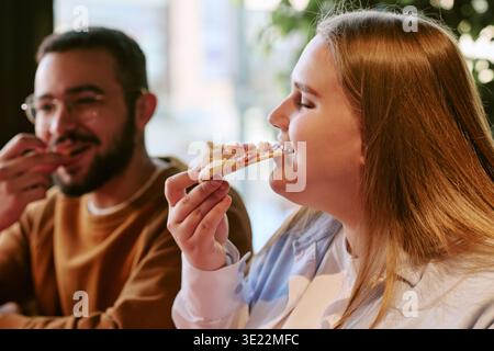 Eine junge Frau genießt Pizza mit einem jungen Mann drinnen Stockfoto