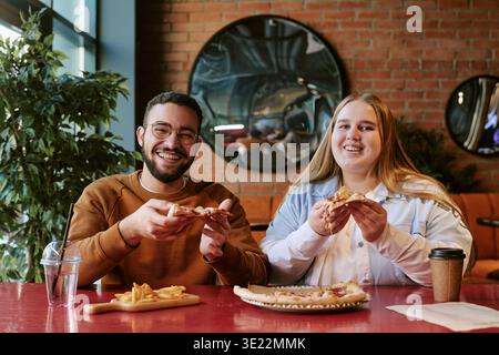 Eine junge Frau und ein Mann aus dem Nahen Osten genießen gemeinsam Pizza drinnen Stockfoto