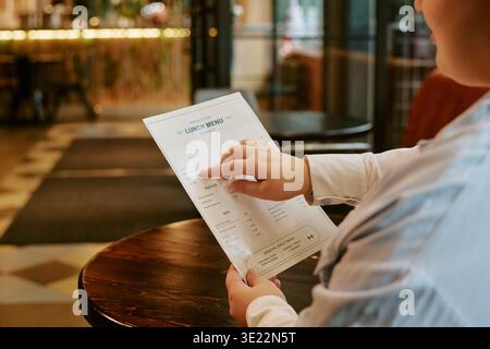 Junge Erwachsene Frau Liest Mittagsmenü, Während Sie Drinnen Sitzt Stockfoto