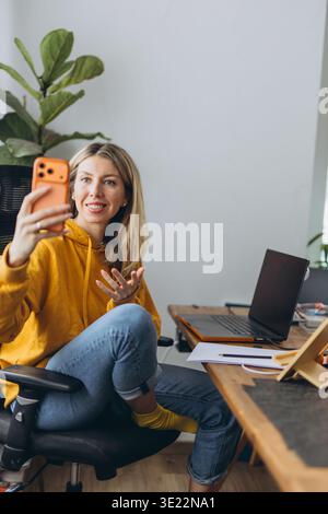 Weibliche Bloggerin, die während eines Online-Anrufs im Home Office Videos auf dem Smartphone aufnimmt, mit Fernkommunikation und digitaler Inhaltserstellung Stockfoto