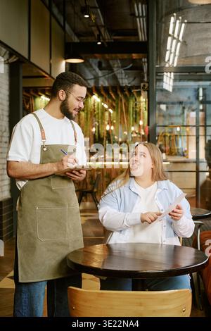 Junge Erwachsene Frau, die Essen von einem Mann mittleren Alters im Cafe bestellt Stockfoto