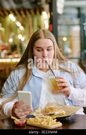 Porträt einer jungen erwachsenen Frau, die Saft trinkt, während sie das Smartphone benutzt Stockfoto