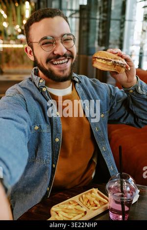 Porträt eines jungen Erwachsenen, der beim Lächeln von Burger im Haus sitzt Stockfoto