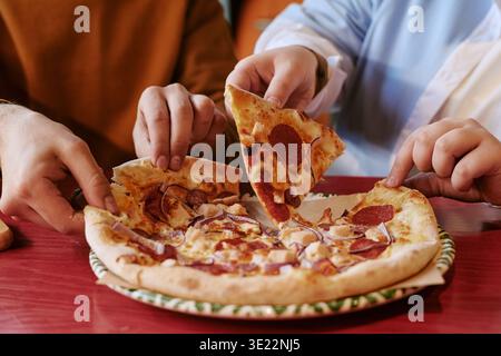 Junge Erwachsene Mann und Frau teilen sich Pepperoni Pizza am Tisch Stockfoto