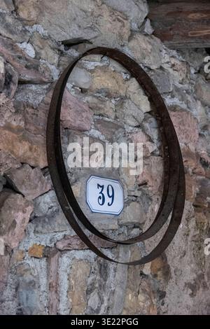 Haus Nr. 39 auf Steinmauer mit Metallring rustikales Detail im Dorf Canale di Tenno, Trentino Südtirol, Italien, 15. März 2026 Stockfoto