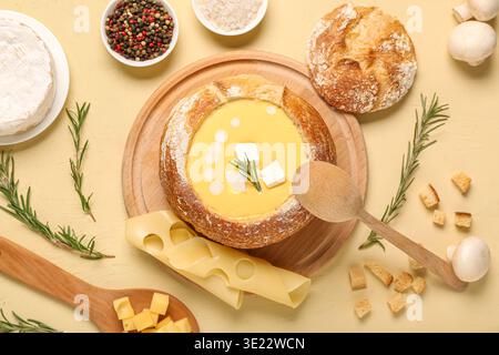 Käsesuppe in Brotschüssel mit Pilzen, Rosmarin und Croutons auf beigefarbenem Hintergrund Stockfoto