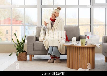Kranke ältere Frau mit Glas Wasser, die zu Hause Kopfschmerzen hat Stockfoto