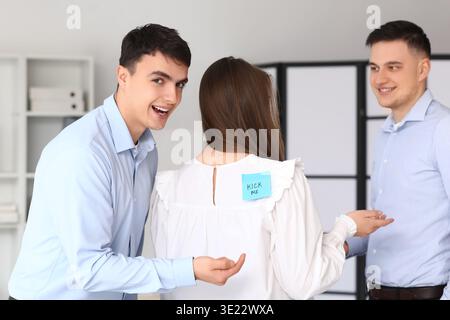 Junge Männer und ihre Kollegin mit klebrigem Papier im Büro. Aprilfeier Stockfoto