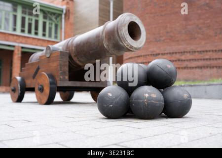 Alte Eisenkanone mit einem Stapel Kanonenkugeln auf einem Stadtplatz. Alte mittelalterliche Artilleriegewehr und schwarze Eisenkugeln im Freien. Stockfoto