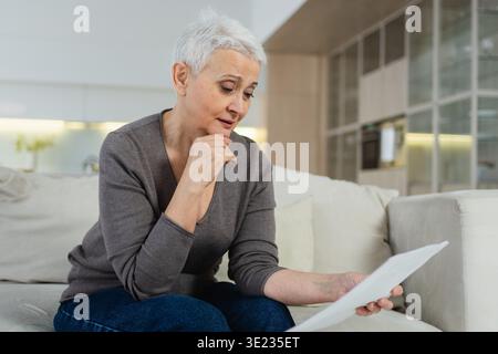 Traurig müde krank krank einsam enttäuschte ältere Frau, die allein zu Hause schlechte Nachrichten liest. Unglückliche reife Großmutter mit Trauer relativer Tod. Gestresste ältere Dame mit Papierkatalog Stockfoto