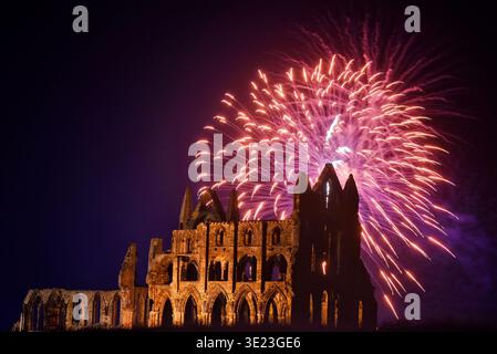 Eine Explosion farbenfroher Lichter erfüllt den Nachthimmel über Whitby Abbey, einem ruinierten Benediktinerkloster an der Küste von North Yorkshire. Diese Szene fand während des großen Finales der Whitby Regatta am 22. August 2017 statt. Die Menschen versammelten sich, um das Feuerwerk zu beobachten, das die Silhouette der Abtei vor der dunklen Kulisse erleuchtete und eine lebendige Atmosphäre schuf. Die Veranstaltung ist bei Einheimischen und Besuchern gleichermaßen beliebt und feiert maritime Kultur und Geschichte entlang der Küste. Stockfoto