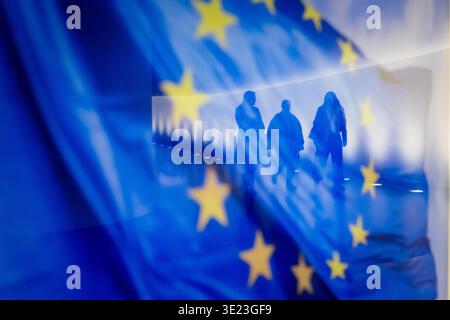 Berlin, Deutschland. März 2026. Die Menschen spiegeln sich in einer europäischen Flagge, wenn sie durch den Verbindungstunnel zwischen Paul Löbe Haus und Reichstagsgebäude laufen. Auf der Tagesordnung der 64. Plenartagung der 21. Legislaturperiode stehen die Erklärung der Bundeskanzlerin zum bevorstehenden EU-Gipfel sowie eine aktuelle Stunde zum Wettbewerb an Tankstellen. Quelle: Christoph Soeder/dpa/Alamy Live News Stockfoto