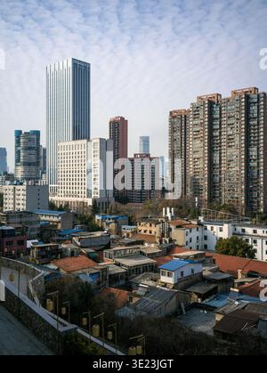 Vertikale Hochwinkelansicht, die den architektonischen Kontrast eines dicht gepackten alten Viertels mit farbenfrohen Dächern vor dem hoch aufragenden modernen Skyscr zeigt Stockfoto