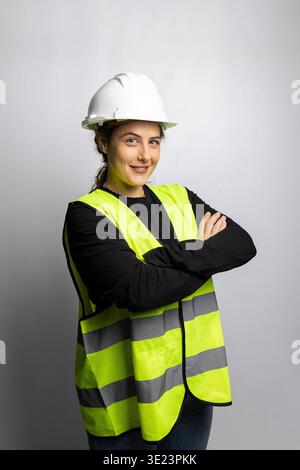 Eine Ingenieurin lächelnd stehend mit überkreuzten Armen, mit weißem Schutzhelm und Sicherheitsweste Stockfoto