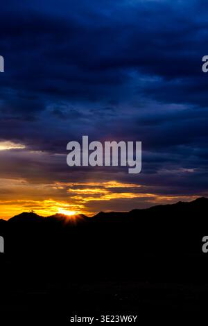 Ein beeindruckender goldener Sonnenuntergang scheint durch die dunklen Berglandschaften und beleuchtet den Horizont mit warmem strahlendem Licht unter einem tiefblauen Himmel Stockfoto