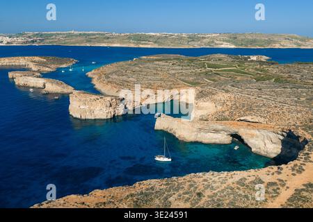 Blick aus der Vogelperspektive auf das türkisfarbene Wasser, das die zerklüfteten Klippen und die karge Vegetation der Blauen Lagune umschließt, Comino, Malta. Stockfoto