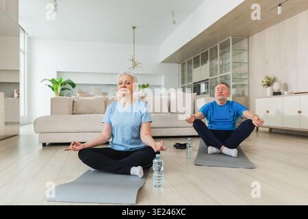 Yoga-Achtsamkeitsmeditation. Älteres erwachsenes Ehepaar, das zu Hause Yoga praktiziert. Die Frau des mittleren Alters sitzt in Lotusposition auf Yogamatte und meditiert entspannend. Familie, die Atemübungen macht Stockfoto