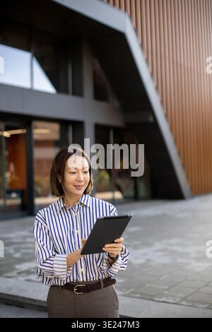 Eine Koreanerin steht vor einem modernen Gebäude. Sie hält eine Tafel und lächelt. Es ist tagsüber und die Gegend ist offen mit einem sauberen Design, Featuri Stockfoto