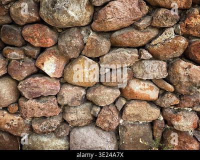 Eine aus nächster Nähe errichtete alte Steinmauer mit unregelmäßig geformten Felsen und Steinen in verschiedenen Farben und Größen Stockfoto