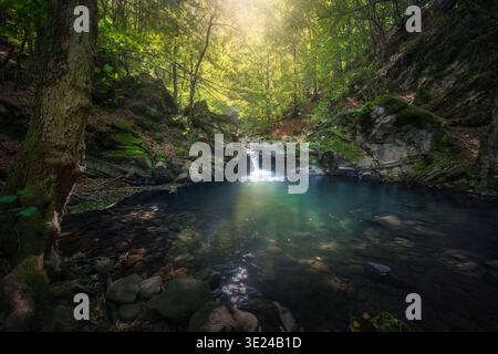 Kleiner Wasserfall mit Sonnenstrahlen, die durch Bäume im Wald von Acquerino filtern. Unberührte Natur in Sambuca Pistoiese, Pistoia, toskanischer Apennin, Italien Stockfoto