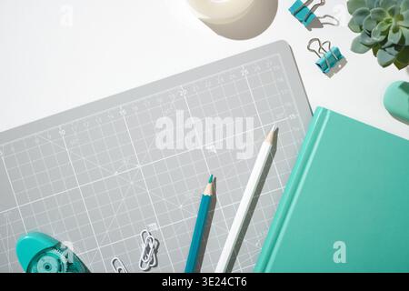Notizbuch in mintfarbener Farbe, Bleistift, Textmarker und Kleber auf grauer Schneidematte. Kopierraum Stockfoto